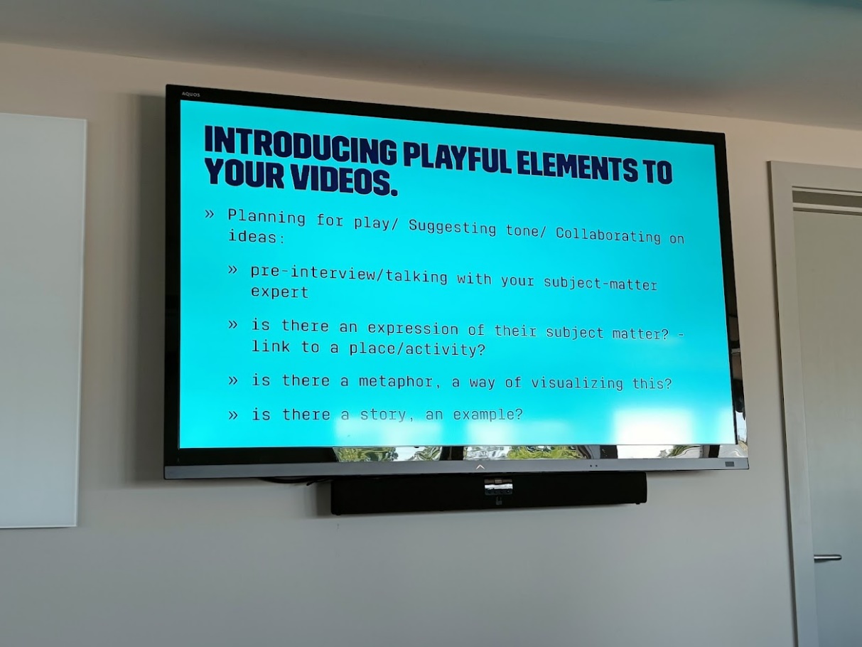 A photograph of a PowerPoint slide, displayed on a screen. The slide reads 'planning for play / suggesting tone / collaborating on ideas. Point 1) pre interview / talking with your subject matter expert. Point 2) is there an expression of their subject matter? Link in to place / activity? Point 3) is there a metaphor, a way of visualising this? Point 4) Is there a story, an example?