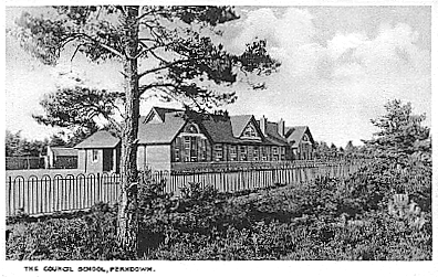 An old black and white photo of a school, with a fence running alongside it and a tree in the foreground