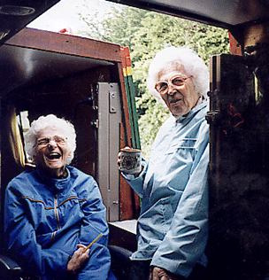 A colour photo of two elderly women, laughing, sitting inside a narrow boat