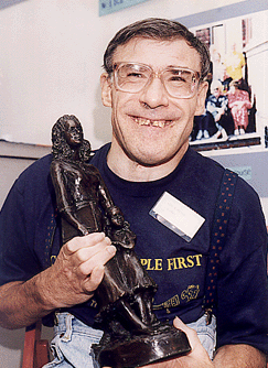 A colour photo of a man holding an award in the shape of a statue