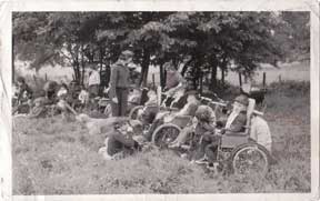 An old black and white photo of a group of people, some in wheelchairs, on the grass in a field