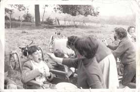 An old black and white photo of women feeding young children in wheelchairs in a field