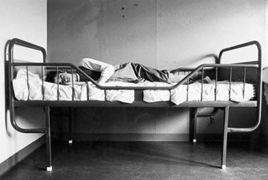 A black and white image of a bed and occupant in a Norwegian institution for people with intellectual disabilities