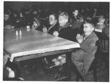 An old black and white photo of children sitting at dining tables in a hall