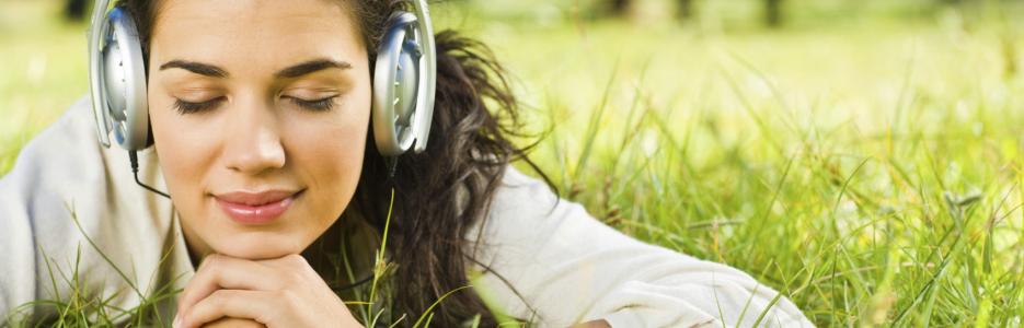 a girl lying on the grass with some headphones on listening to some audio.