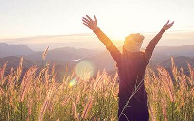 Woman standing in a meadow with arms outstretched, at sunrise