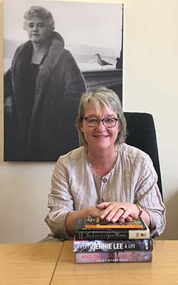 OU in Scotland Director Susan Stewart seated with a pile of favourite books. A picture of Jennie Lee is on the wall. 