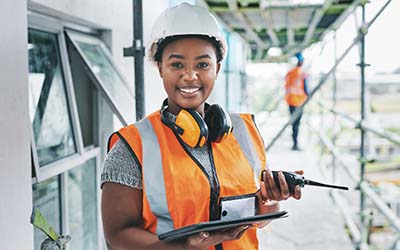 A woman on a construction site holding a digital tablet and walkie talkie 
