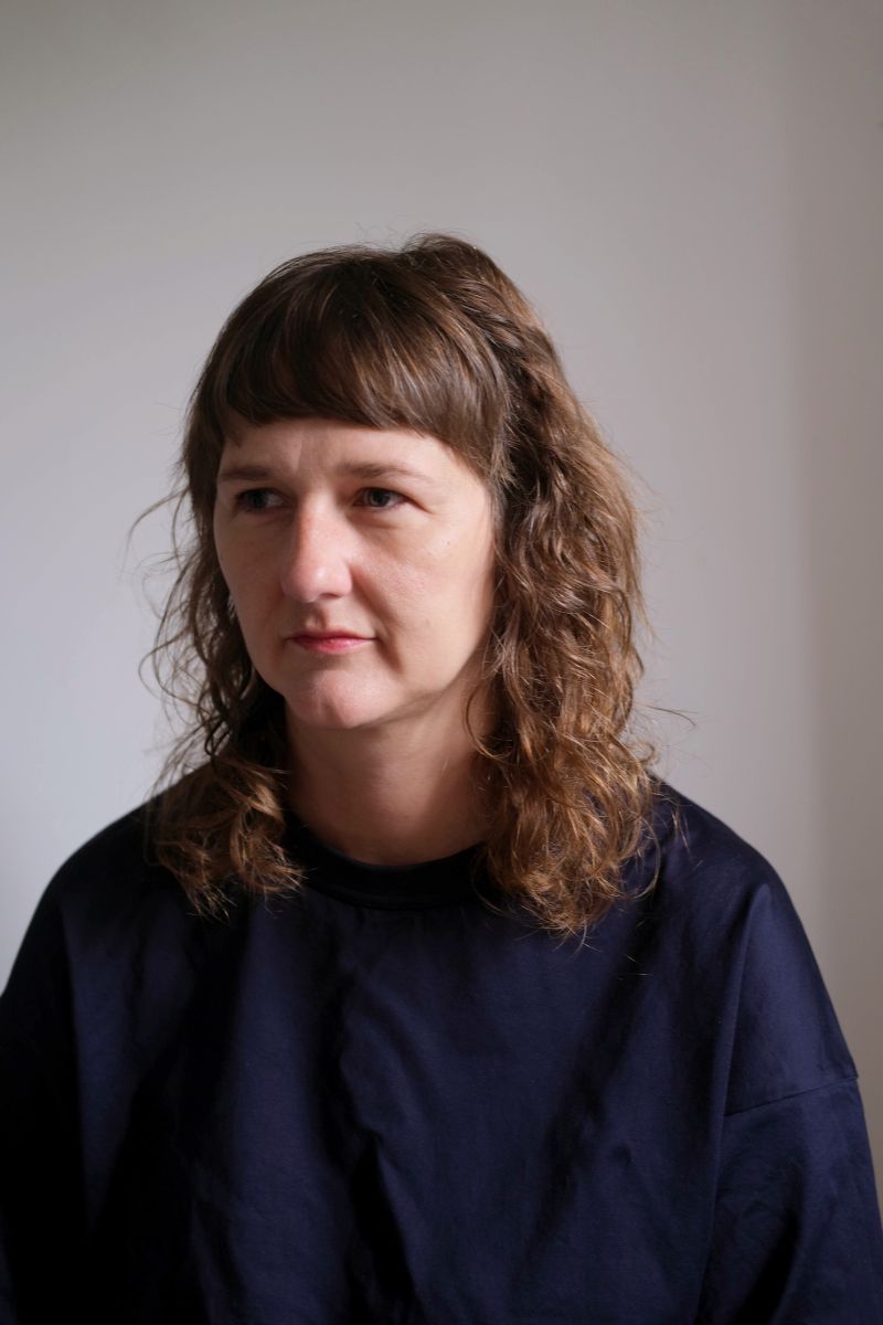 Portrait photograph of writer Clare Pollard, wearing dark blue jumper and looking away from the camera towards the left.