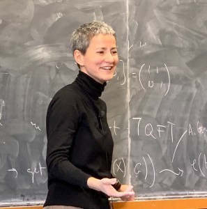 A photo of Marina Logares standing in front of a whiteboard with mathematics written on the board. Marina is smiling. 