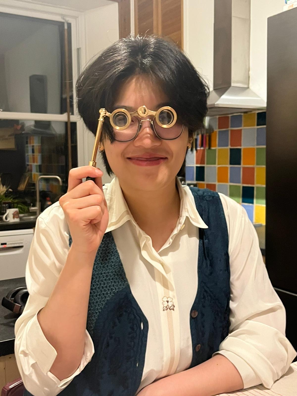 A photo of Xinyi holding up a pair of metal spectacles. 