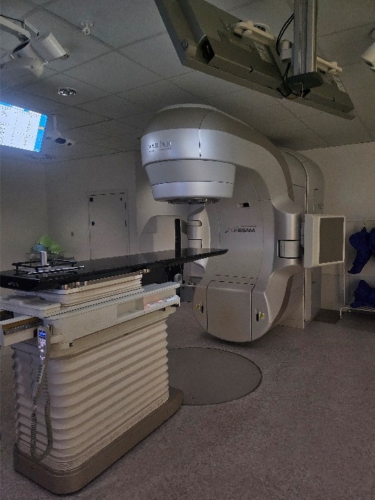 A room height medical machine connected to a control desk and display screen.