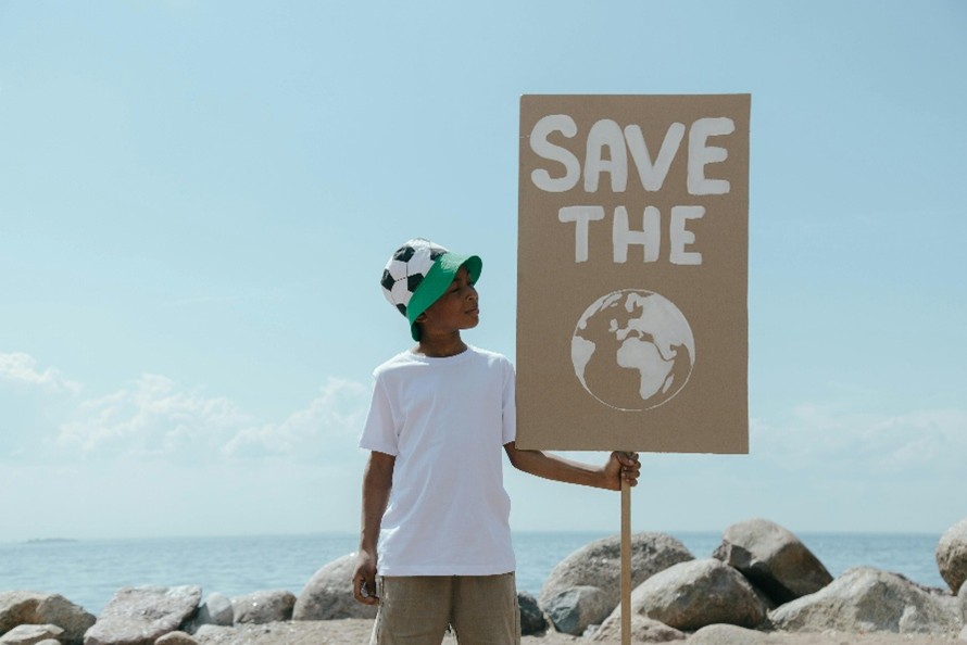 Photo of a boy on a beach in a football hat holding up a sign saying 'save the' with a picture of the planet under the text