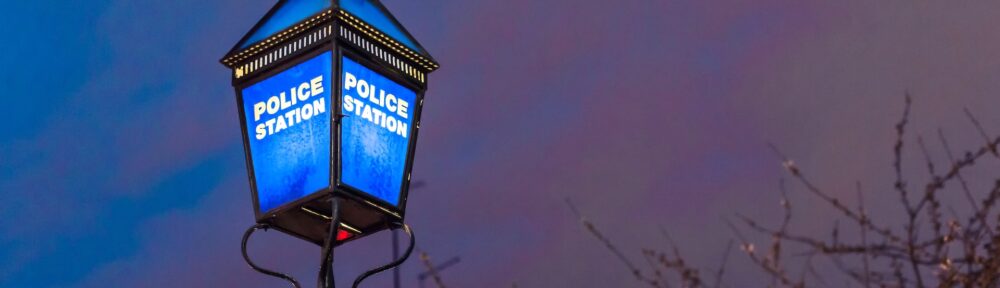 A police lantern. The lantern is lit up at night with the words police station in white letters on a blue background.