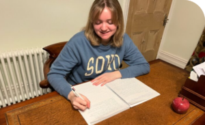 Image of student Chloe writing at her desk.