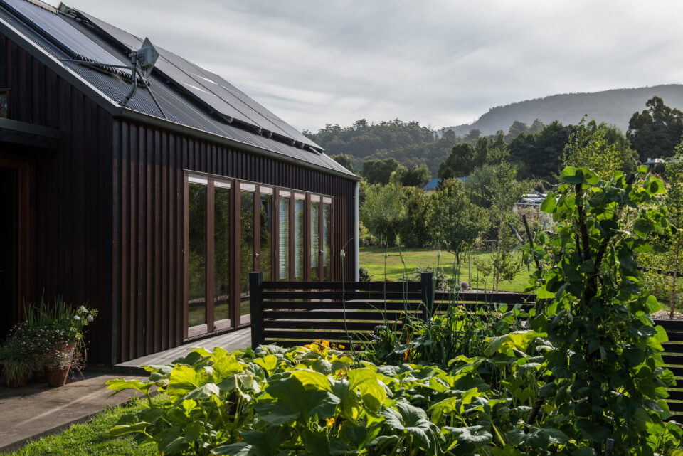 Northern elevation of the house that feeds with glazing for solar gain, rooftop solar panels and productive garden in foreground.