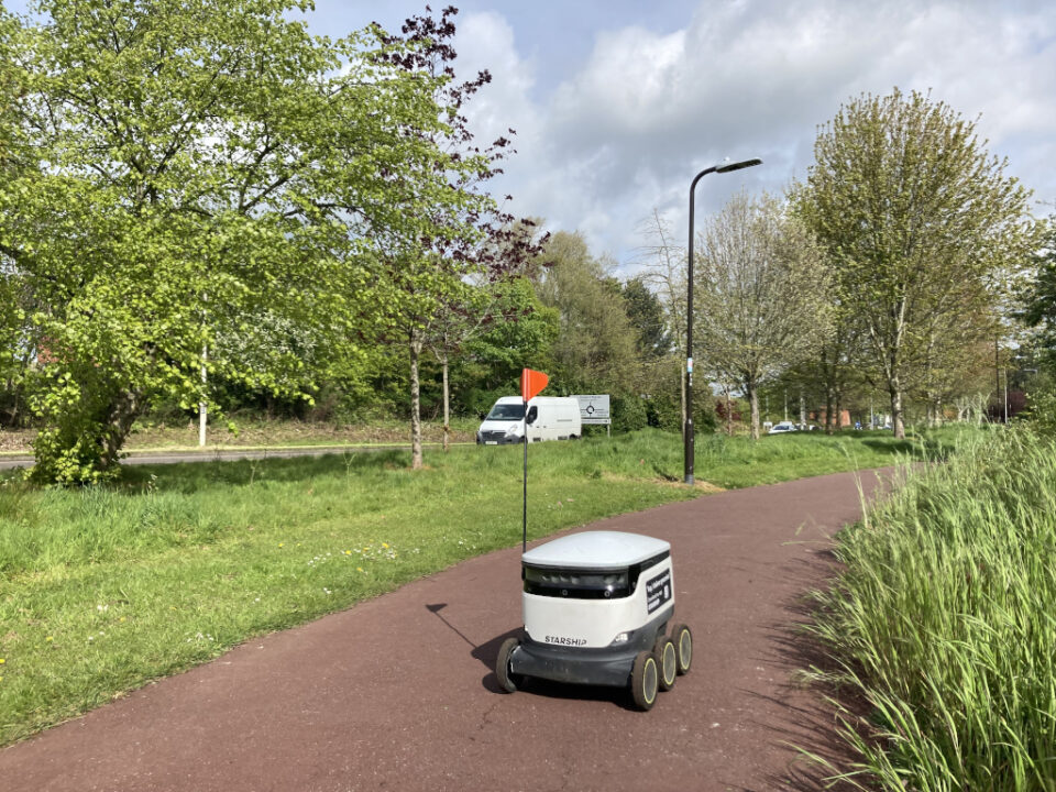 A delivery robot in a segregated pedestrian footpath, separated from the road by a strip of grass