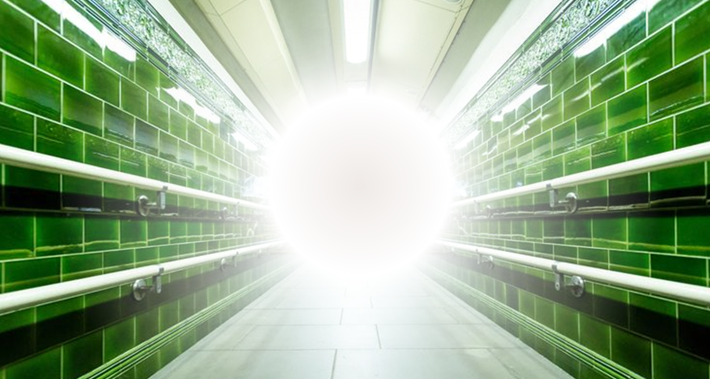 ALT TEXT: A visual representation of sensory overwhelm in an underground train station tunnel: a bright light or aura in the centre of the image impedes wayfinding.