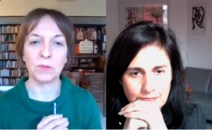 A middle-aged caucasian woman in a green rollneck top sits in front of bookcases. She's talking on a Zoom call to a middle-aged Asian woman, who is sitting closer to the screen.