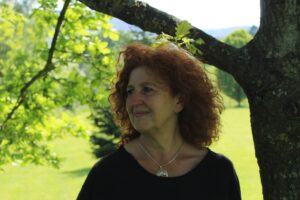 A headshot of Gwyneth Jones, a Caucasian woman with curly ginger hair, wearing a round neck black blouse and a silver necklace with a silver pendant. 