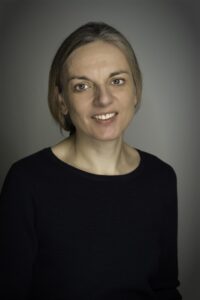 Headshit image of a middle-aged woman with blonde hair in a ponytail wearing a black crew neck t-shirt