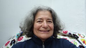 A woman with chin-length grey curly hair smiles into the camera. 
