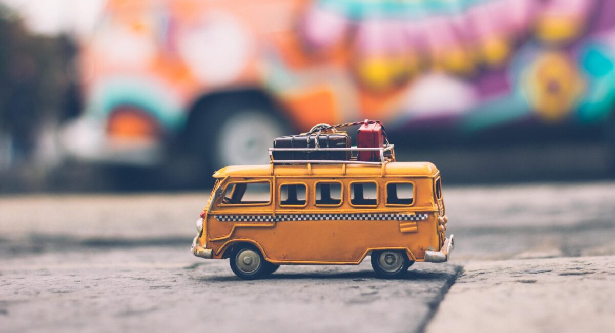 Image of a model yellow van with suticases on the roof. The photo is taken using the tilt-shift method, which makes it look even more miniature.