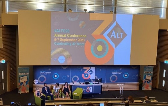 View of speakers and the big screen in the conference space at the ALT conference. The screen reads '#ALTC23 Annual Conference; 5-7 September 2023; Celebrating 30 years'. There are 4 speakers on the stage under the screen.
