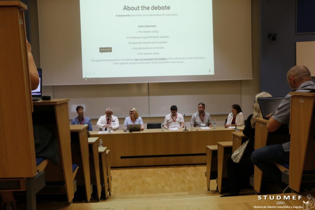 The iLED debate panel seen in a lecture hall. There are people with laptops in the audience watching the activity.