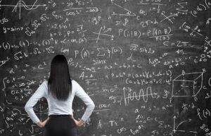 Rear view of a thoughtful woman who tries to solve math problems. Math calculations on black chalk board. Thinkstock