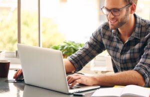 Young man, wearing glasses and smiling, as he works on his laptop