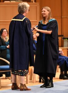 A young woman dressed in graduation robes, receiving her degree certificate.