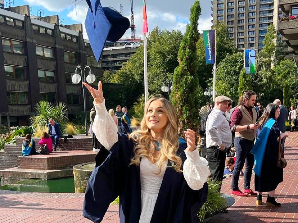 Young girl with long blonde hair throwing a mortar board in the air.