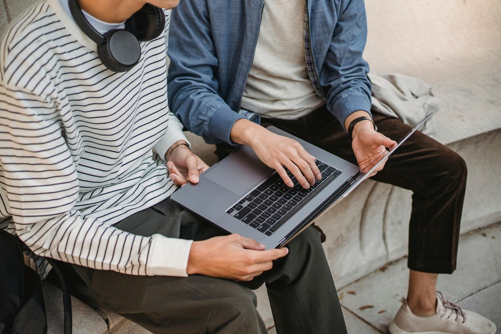 Two young men collaborating on a laptop outdoors, focusing on digital learning and teamwork