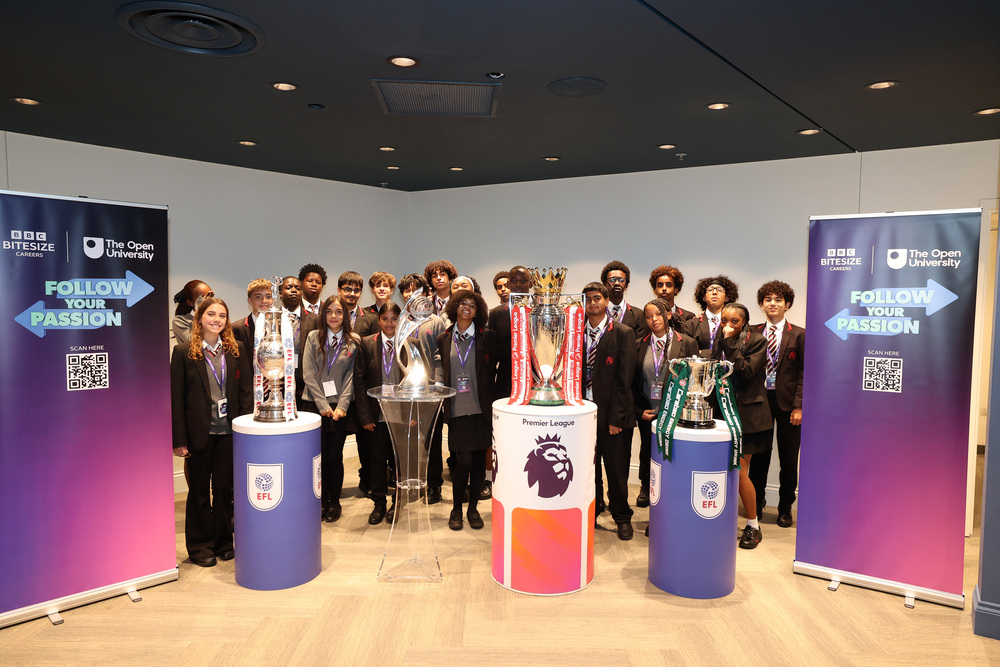 Students pose beside the Premier League trophy and other football trophies at the BBC Bitesize Careers Follow Your Passion event, with campaign banners from BBC Bitesize Careers and The Open University displayed on either side.