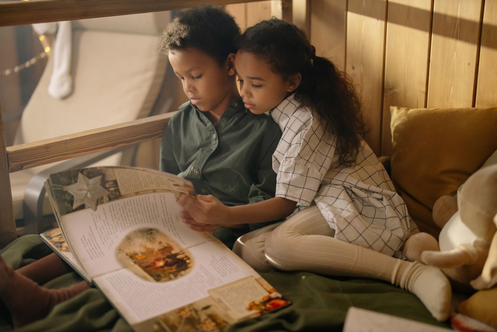 Two kids enjoy reading a book together in a warm and cozy bedroom setting