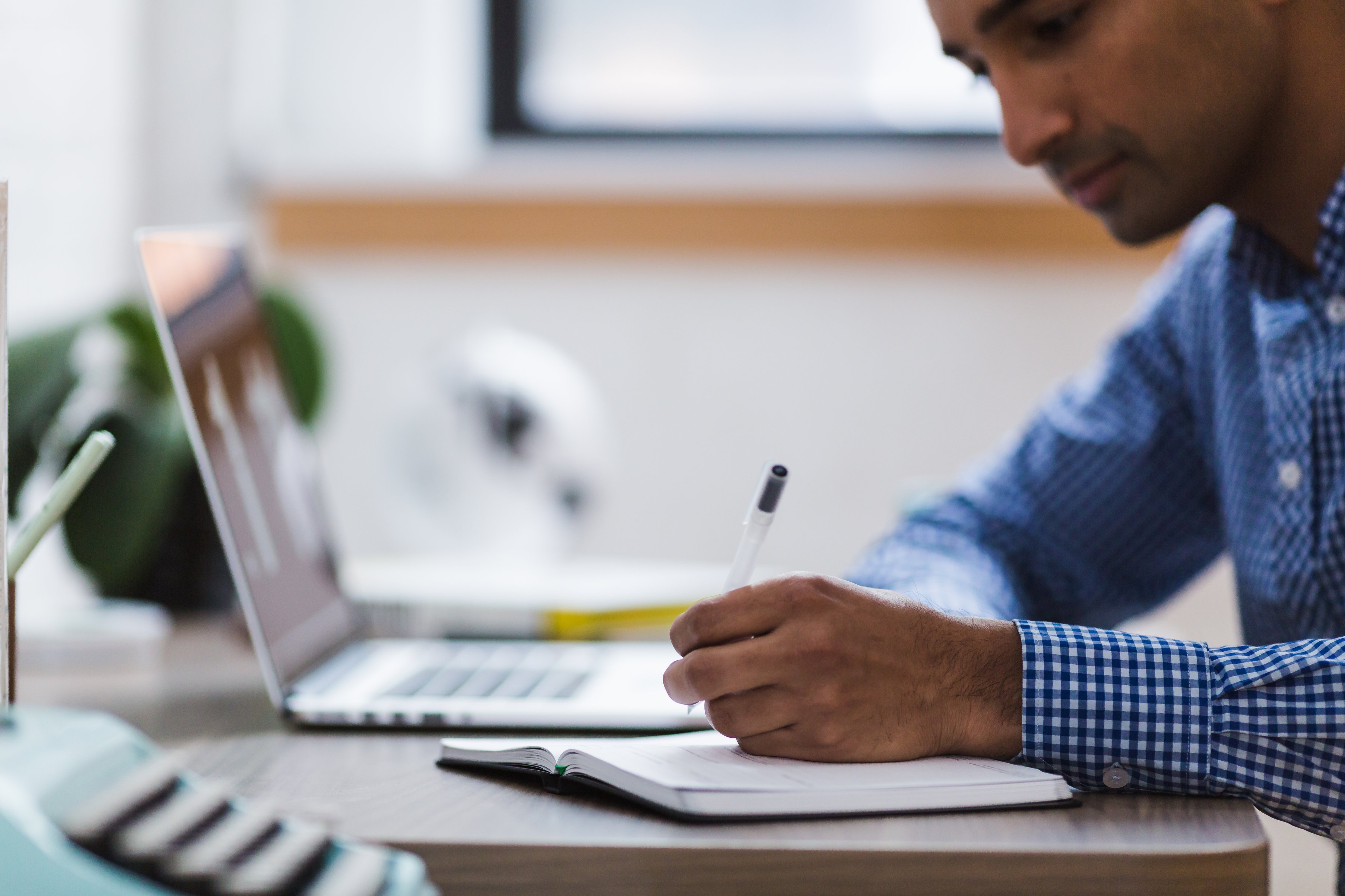 Image shows a man looking at laptop and writing notes (image credit: Stock snap, Pixabay)