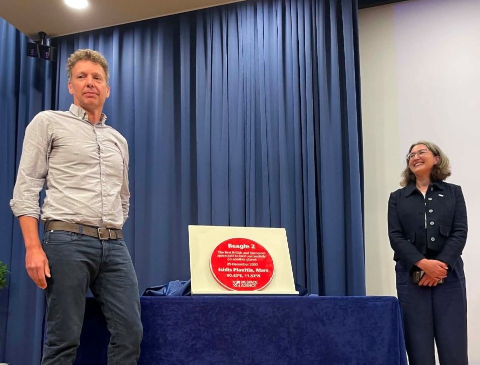 Image of the unveiling of the plaque showing Nicolas Pillinger standing on the left and Julie Black, from the UK Space Agency on the right with the plaque on the table in the middle. Copyright The Open University