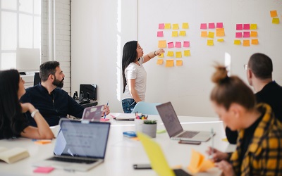 Photo by You X Ventures on Unsplash - photo shows a team of colleagues in a meeting, using a whiteboard covered in post-it notes