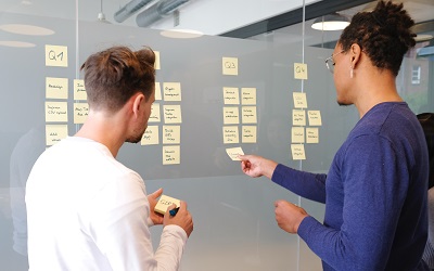 Two professionals use a large board and sticky notes for collaborative work