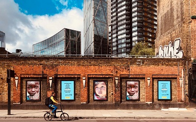 Photo by Étienne Godiard on Unsplash - images shows a cyclist riding past charity adverts on a brick wall in London. The wall looks run down and tired and behind it, beautiful modern, imposing sky scrapers. The image reflects the challenges faced by charities and the disparity between the support the private sector has received during the pandemic and the limited support the voluntary sector has received