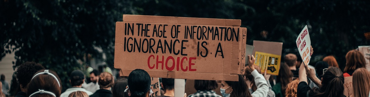 A protestor's sign reads "In the age of information ignorance is a choice"