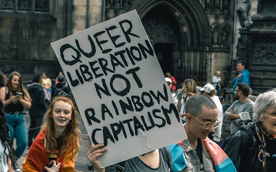 A sign at an LGBTQI protest reads "Queer Liberation not Rainbow Capitalism". The protest is outside Westminster Cathedral in London, UK and was taken in 2019