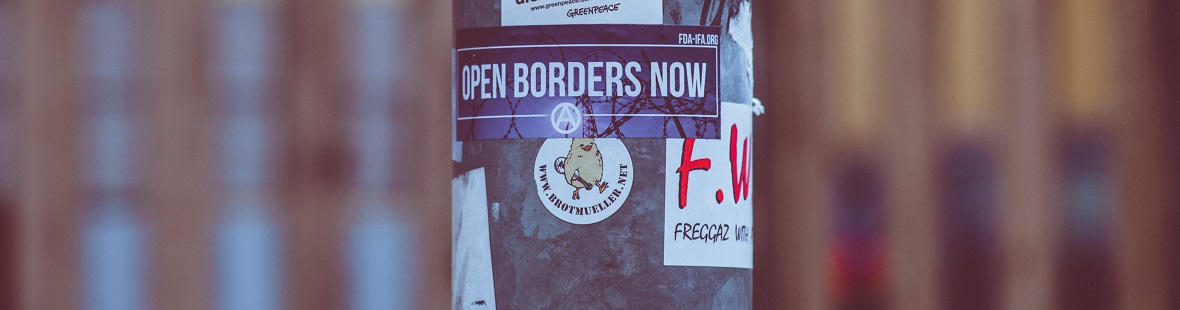 A poster on the street reads "open borders now"