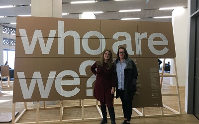 Two members of the research team stand infront of a sign which says "Who are we?"