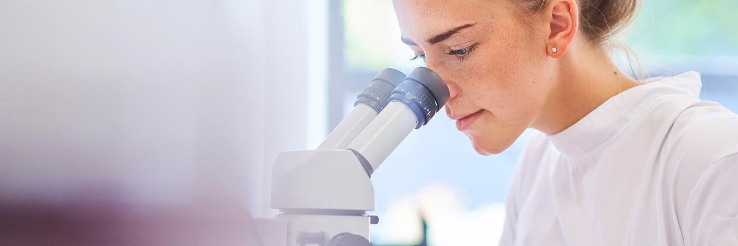 Chemistry certificate graduate using a microscope.