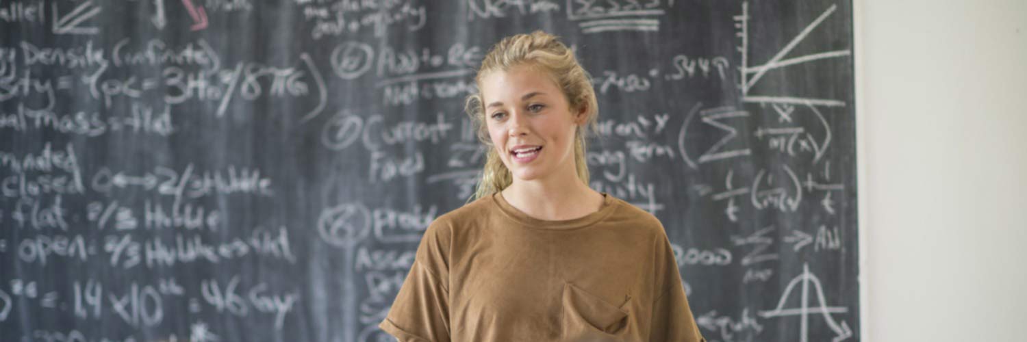 Young woman presenting in front of a blackboard showing maths equations