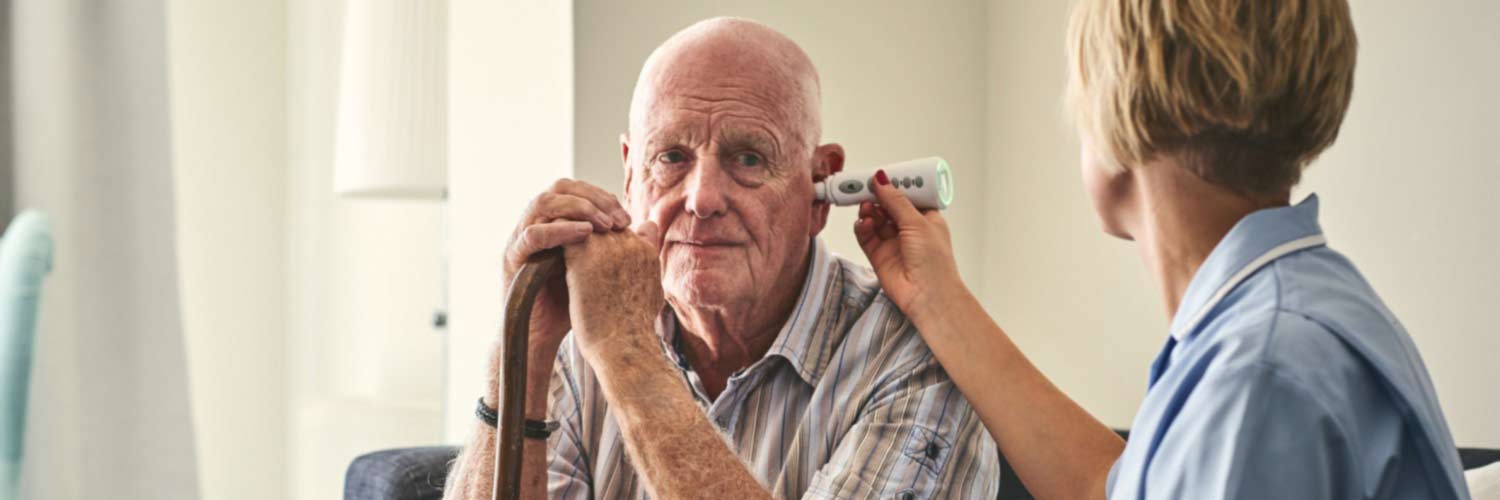Female nurse uses a digital ear thermometer with older male patient