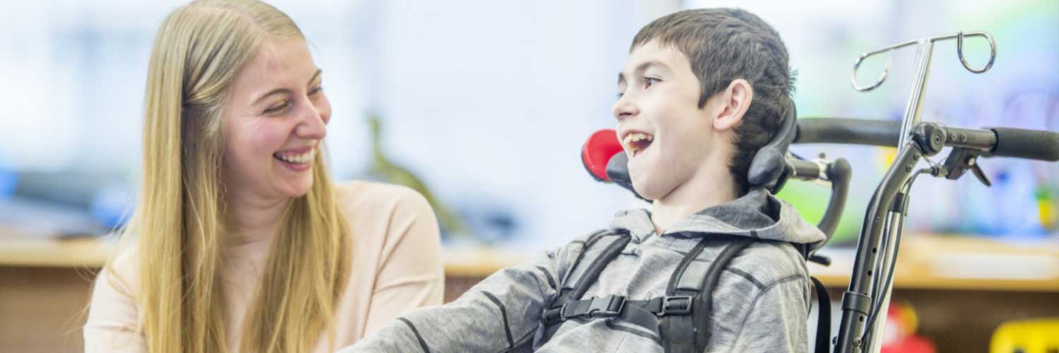 Boy in wheelchair laughing with young woman