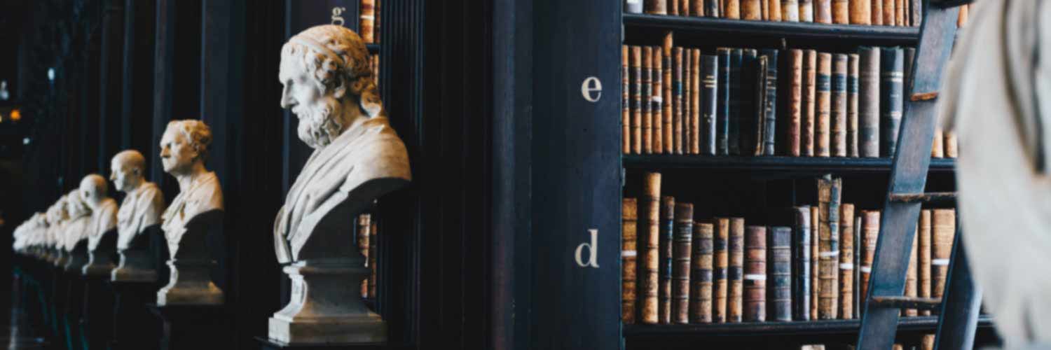 Interior view of library shelves and row of stone busts of philosophers